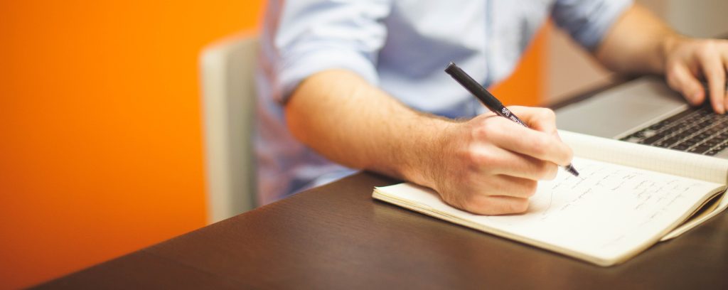 Man at computer, taking notes and learning